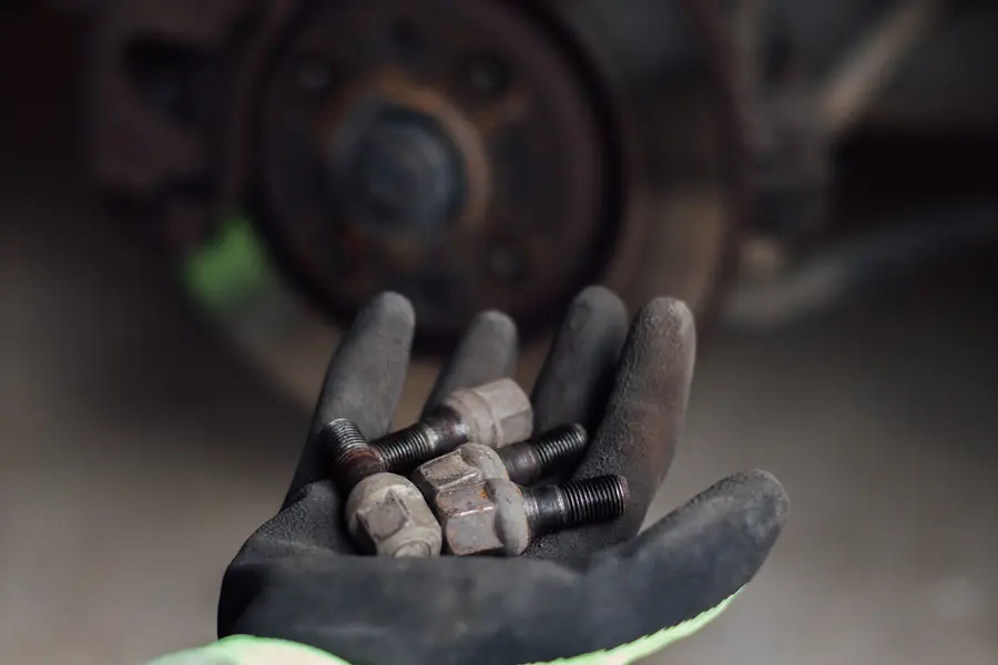 Lug nuts held in a gloved hand next to a wheel hub