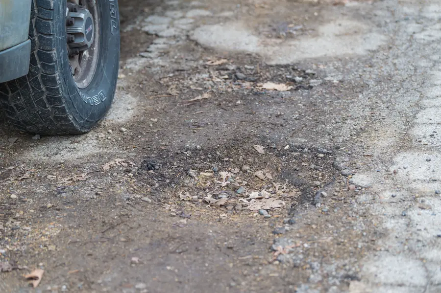 A car tire next to a broken-up pothole, the kind of hit that knocks a wheel out of alignment